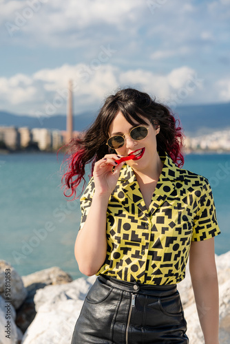 Vertical shot of a modern Caucasian woman eating a red liquorice candy against the backdrop of a sea. photo