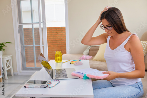 beautiful and young woman studying on sofa at home with laptop and taking notes