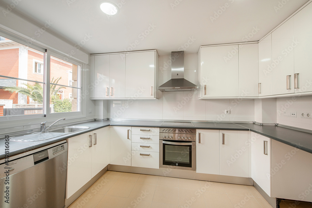 Fototapeta premium Large kitchen with bright white cabinets, stainless steel appliances and gray material countertop