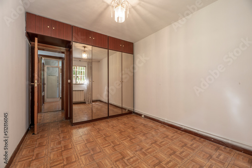 Bedroom with wall lined in wooden fitted wardrobes with matching chests and four mirror covered doors