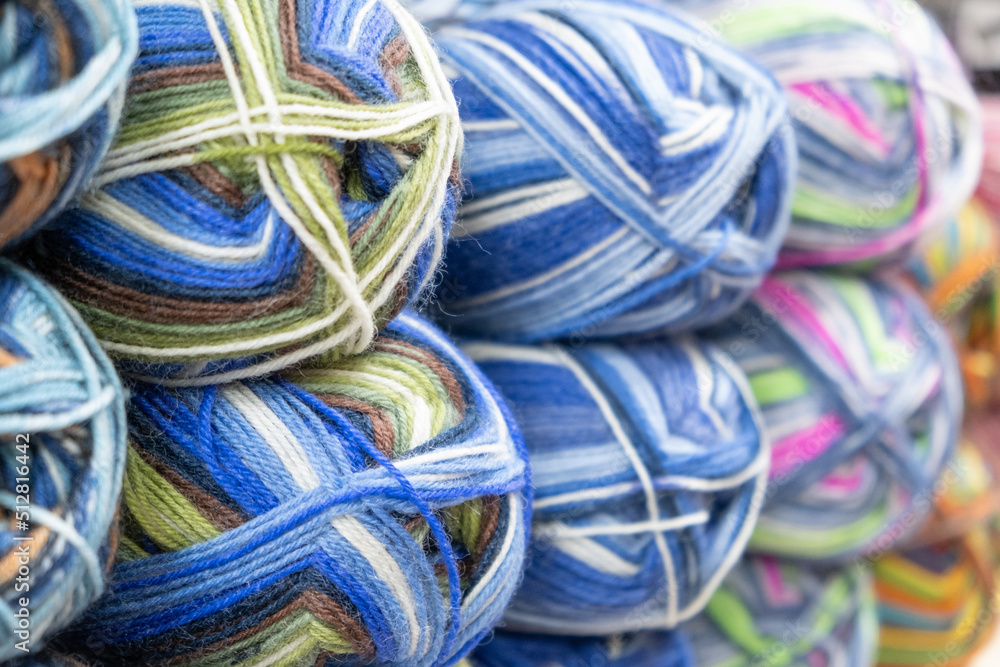 Many multi-colored balls of yarn for knitting on a shelf in a needlework store, close-up, selective focus