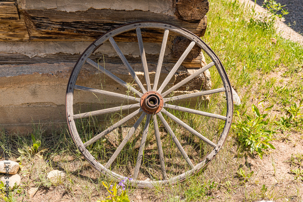 Old weathered wagon wheel leaning against a log cabin wall
