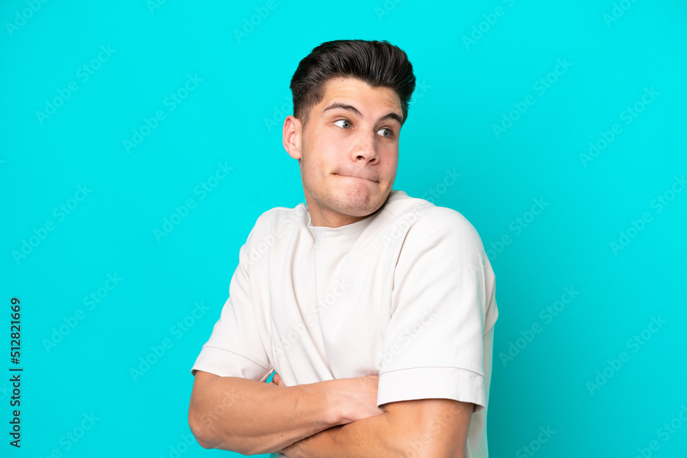 Young handsome caucasian man isolated on blue bakcground making doubts gesture while lifting the shoulders Young handsome caucasian man isolated on blue bakcground making doubts gesture while lifting the shoulders