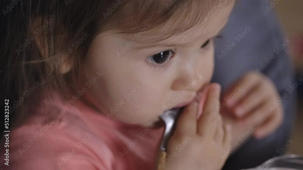 Cute baby girl biting a spoon while sitting on high-chair. Healthy food. Beautiful closeup portrait. Beautiful young girl. Cute baby girl biting a spoon while sitting on high-chair. Healthy food. Beautiful closeup portrait. Beautiful young girl.
