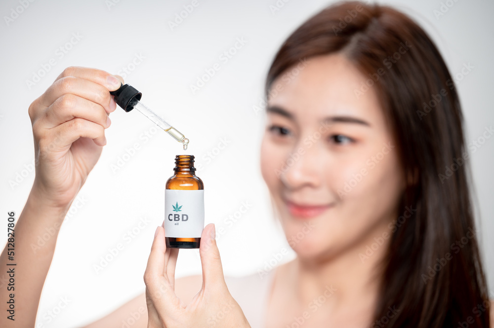 close up asian woman looks at a bottle of CBD oil. Sleep supplement. Medical marijuana. vitamins and supplements healthy alternatives.. close up asian woman looks at a bottle of CBD oil. Sleep supplement. Medical marijuana. vitamins and supplements healthy alternatives..