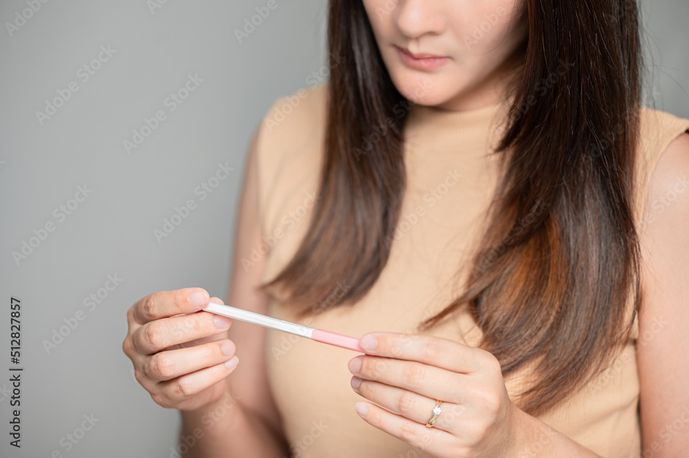 Asian woman holding pregnancy test feeling disappointed by negative result female health problems and infertility. or unwilling pregnancy, abortion. Asian woman holding pregnancy test feeling disappointed by negative result female health problems and infertility. or unwilling pregnancy, abortion.