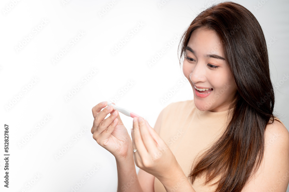 Asian woman holding pregnancy test feeling happy by positive result. female health problems and infertility. successful treatment IUI Intra – Uterine Insemination and ICSI
