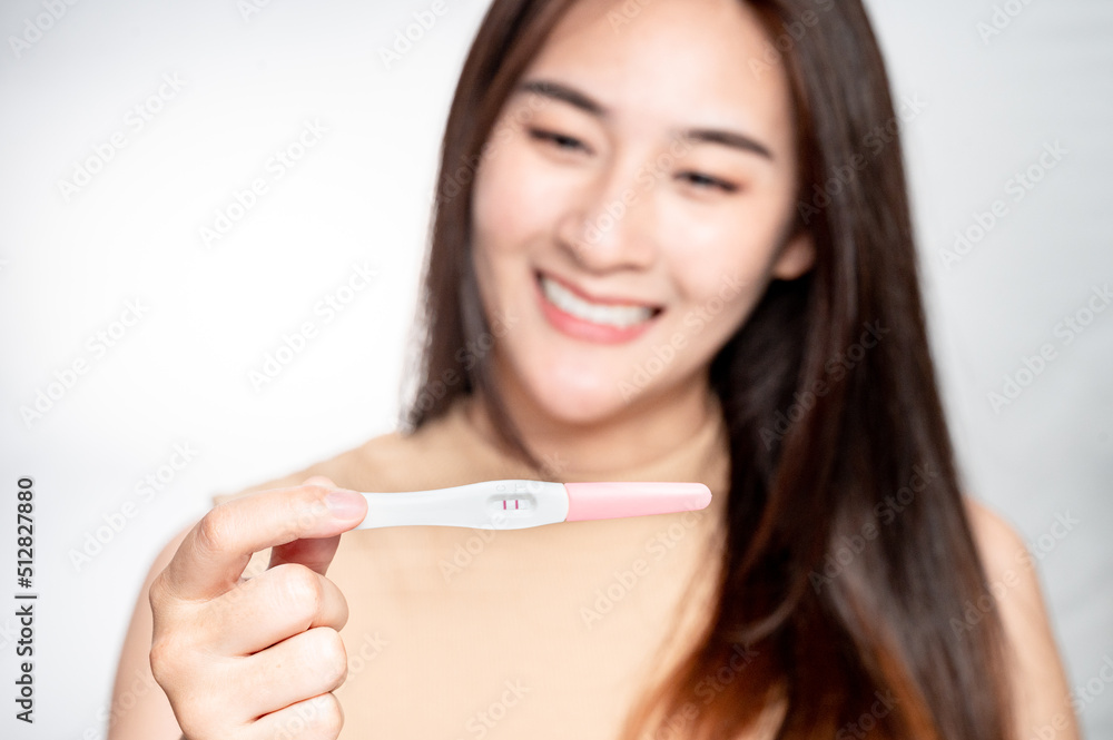 Asian woman holding pregnancy test feeling happy by positive result. female health problems and infertility. successful treatment IUI Intra – Uterine Insemination and ICSI Asian woman holding pregnancy test feeling happy by positive result. female health problems and infertility. successful treatment IUI Intra – Uterine Insemination and ICSI