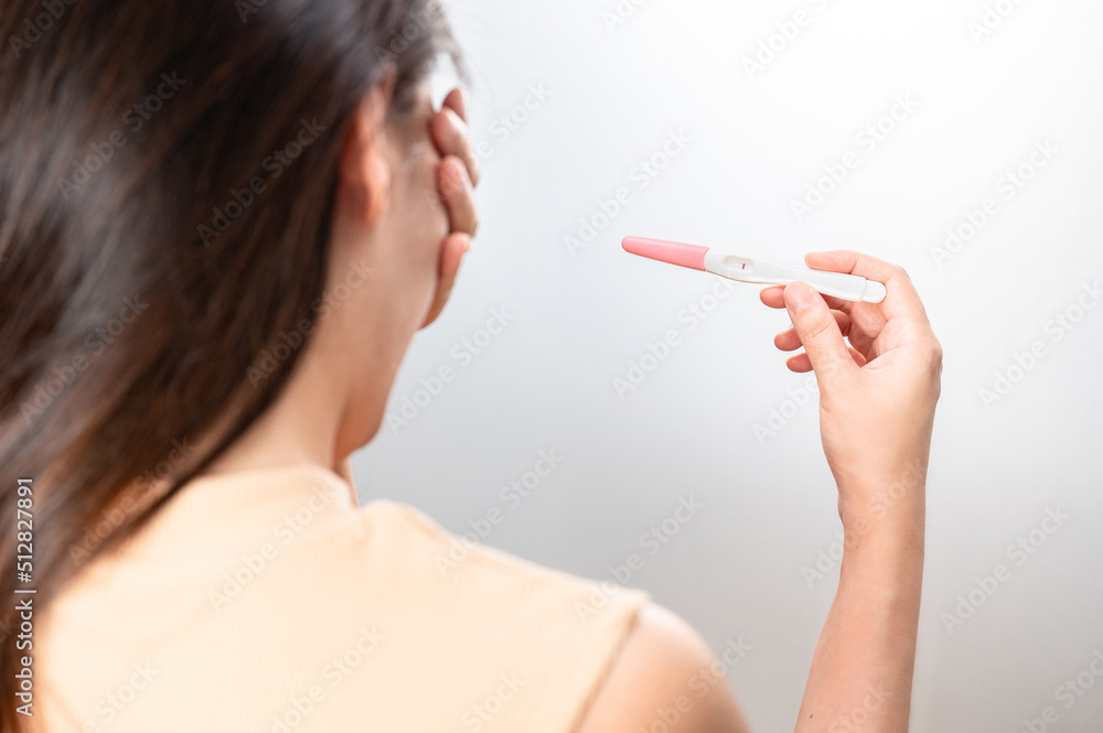 Asian woman holding pregnancy test feeling disappointed by negative result female health problems and infertility. or unwilling pregnancy, abortion. Asian woman holding pregnancy test feeling disappointed by negative result female health problems and infertility. or unwilling pregnancy, abortion.