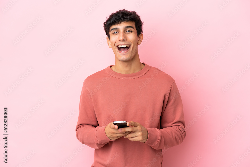 Young Argentinian man isolated on pink background surprised and sending a message Young Argentinian man isolated on pink background surprised and sending a message