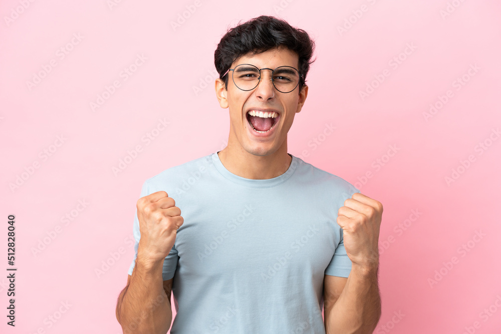 Young Argentinian man isolated on pink background With glasses and celebrating a victory Young Argentinian man isolated on pink background With glasses and celebrating a victory