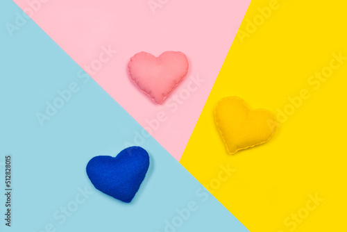 Corazones de colores de tela hecho a mano sobre un fondo rosa, amarillo y celeste liso y aislado. Vista superior y de cerca. Copy space