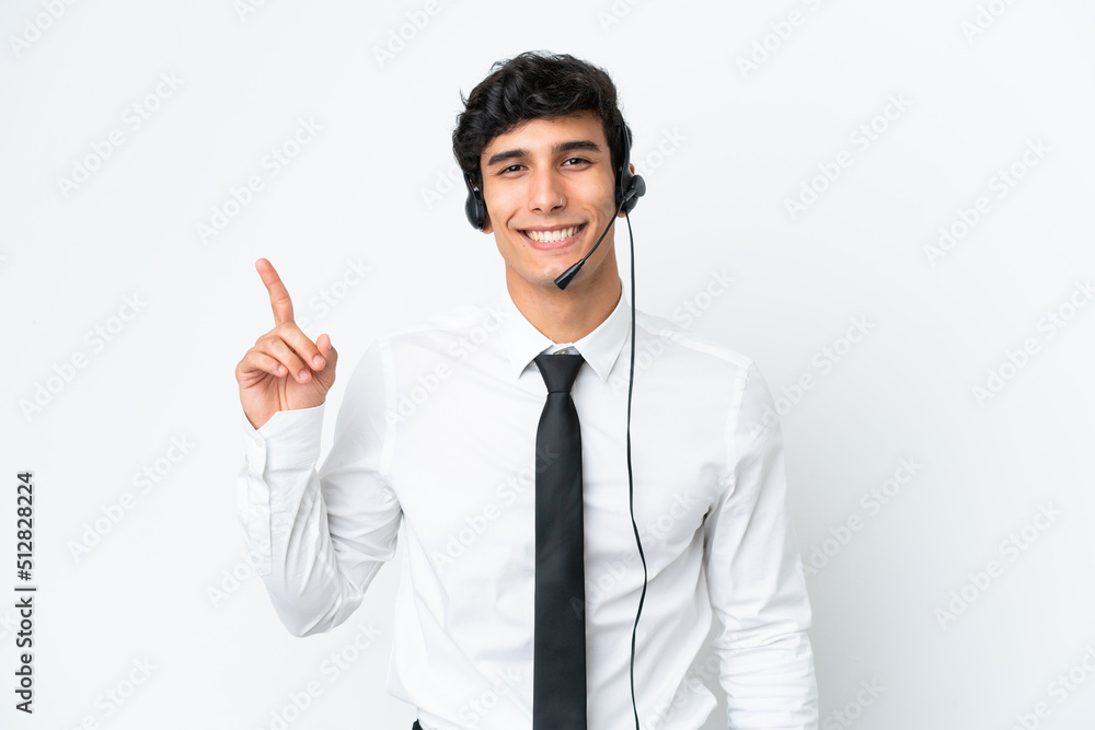 Telemarketer man working with a headset isolated on white background showing and lifting a finger in sign of the best
