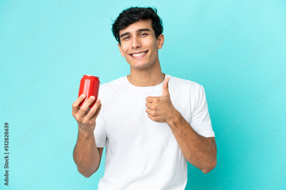 Young Argentinian man holding a refreshment isolated on blue background giving a thumbs up gesture