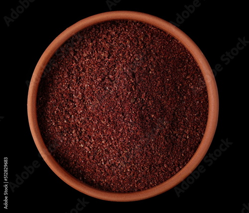 Ground sumac spice, pile in clay pot isolated on black, top view  photo