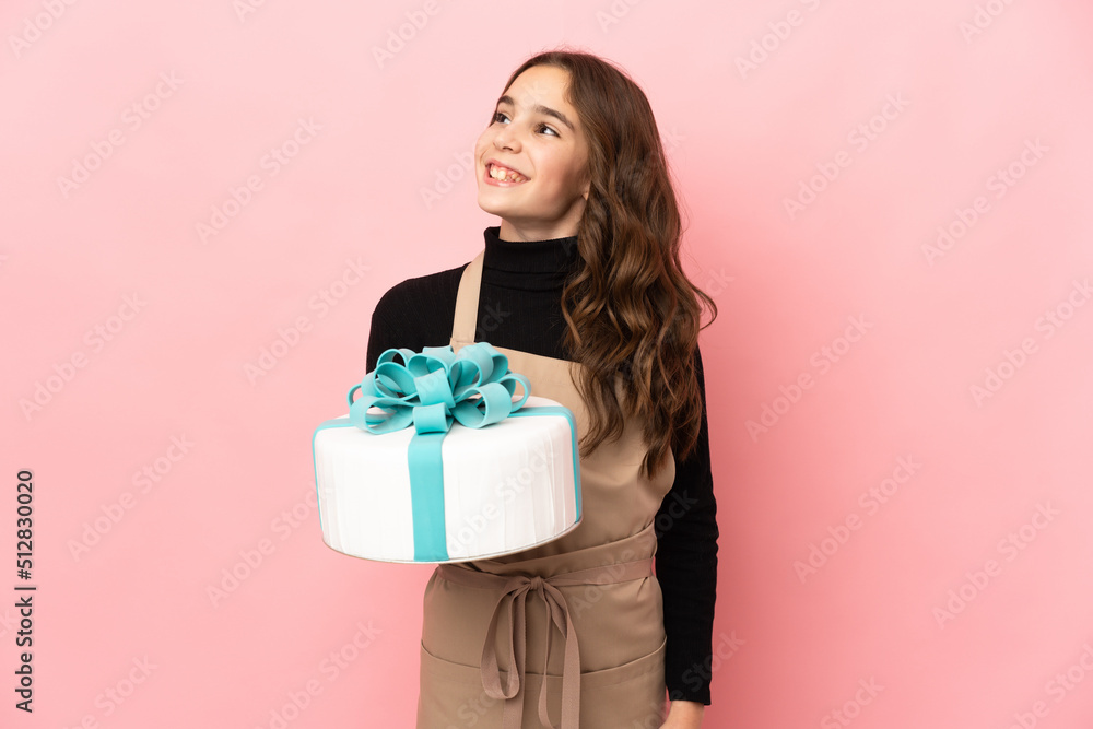 Little Pastry chef holding a big cake isolated on pink background thinking an idea while looking up Little Pastry chef holding a big cake isolated on pink background thinking an idea while looking up