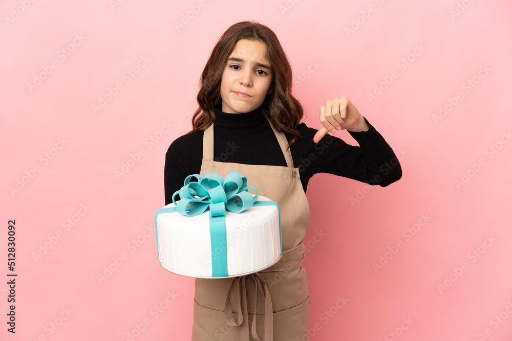 Little Pastry chef holding a big cake isolated on pink background showing thumb down with negative expression Little Pastry chef holding a big cake isolated on pink background showing thumb down with negative expression