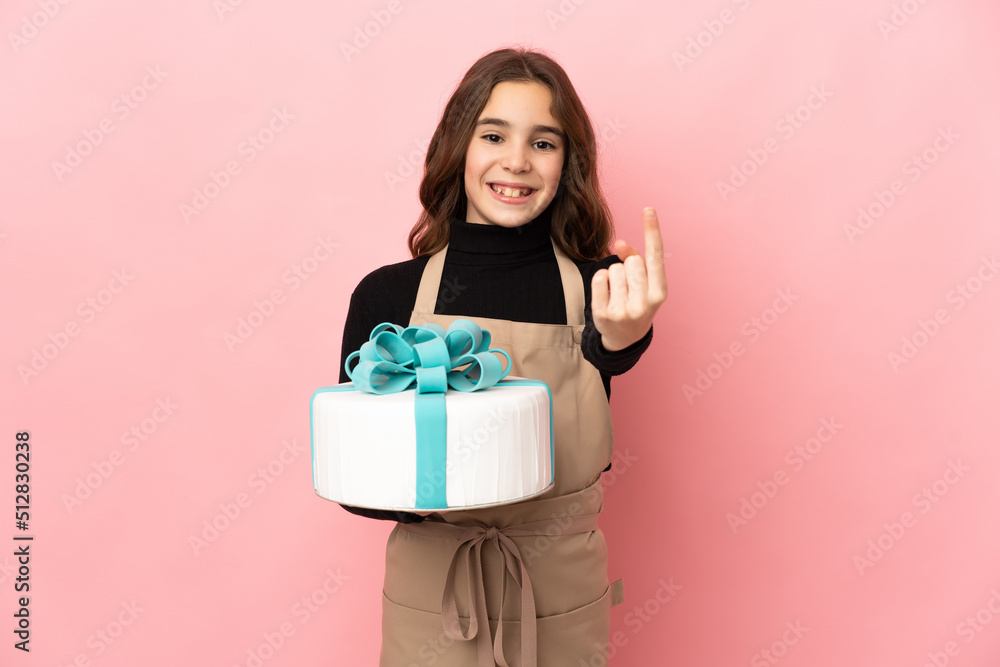 Little Pastry chef holding a big cake isolated on pink background doing coming gesture Little Pastry chef holding a big cake isolated on pink background doing coming gesture