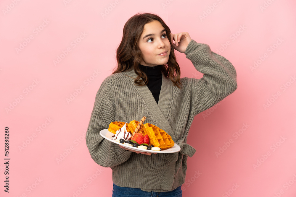 Little girl holding waffles isolated on pink background having doubts and thinking Little girl holding waffles isolated on pink background having doubts and thinking