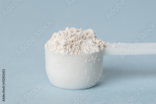 Diatomaceous earth or diatomite powder in a plastic spoon on a blue background. Close up of white powder in a scoop photo