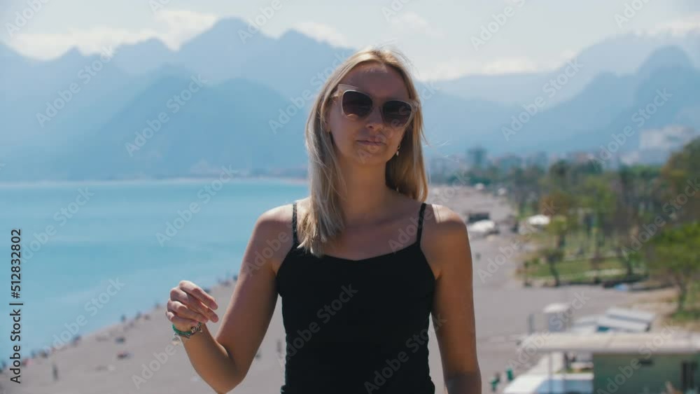 Blonde woman standing on the background of a beach and takes off her sunglasses Blonde woman standing on the background of a beach and takes off her sunglasses