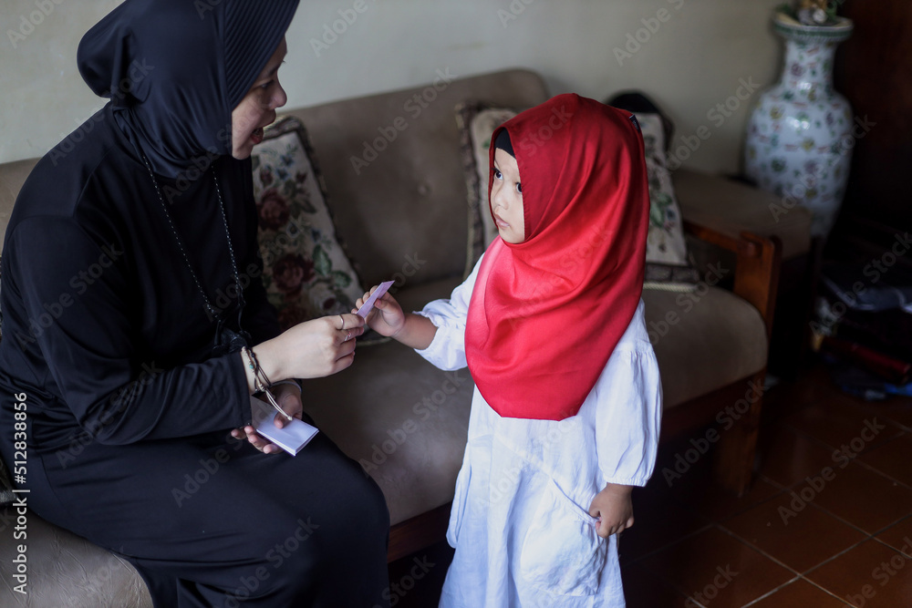 Indonesian people tradition during Eid Mubarak celebration of distributing money or called THR. Asian muslim woman give money to cute girl of family during Idul Fitri. 