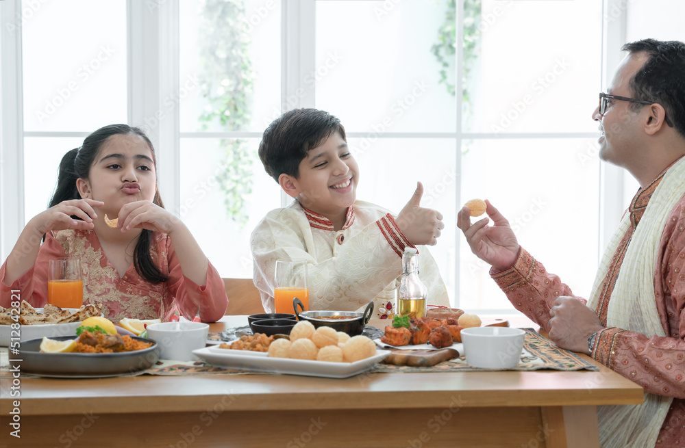 Happy Indian family enjoy eating food with hands, South Asian father and children wear traditional clothes, sitting at dining table at home together. Indian culture lifestyle. Happy Indian family enjoy eating food with hands, South Asian father and children wear traditional clothes, sitting at dining table at home together. Indian culture lifestyle.