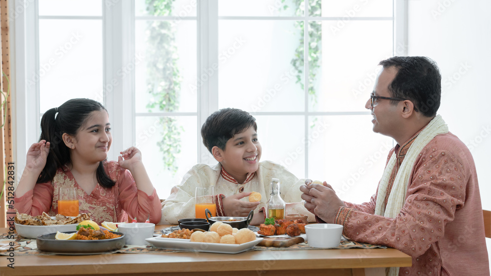 Happy Indian family enjoy eating food with hands, South Asian father and children wear traditional clothes, sitting at dining table at home together. Indian culture lifestyle.