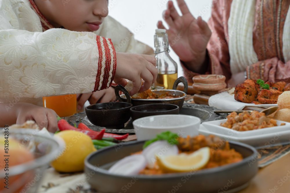 Selective focus on Indian boy hand holding naan bread dipping curry in dish enjoy eating food with hands, wearing traditional clothes, sitting with family at dining table. Indian culture lifestyle Selective focus on Indian boy hand holding naan bread dipping curry in dish enjoy eating food with hands, wearing traditional clothes, sitting with family at dining table. Indian culture lifestyle