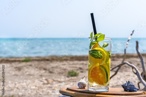 Detox infused water with lime, oranges, mint in glass on the beach with sea coast view