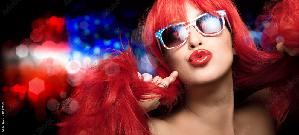 Obraz premium Sexy woman with red hair wearing American flag sunglasses, celebrates 4th July, pouting her beautiful plump lips at camera