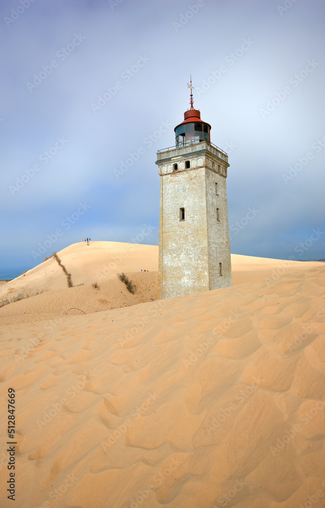 Lighthouse on a sand dune by the sea against a blue sky. Mysterious old tower alone in the desert. Deserted lighthouse isolated on beige sand. Peaceful and tranquil nature scene in Jutland, Denmark. Lighthouse on a sand dune by the sea against a blue sky. Mysterious old tower alone in the desert. Deserted lighthouse isolated on beige sand. Peaceful and tranquil nature scene in Jutland, Denmark.