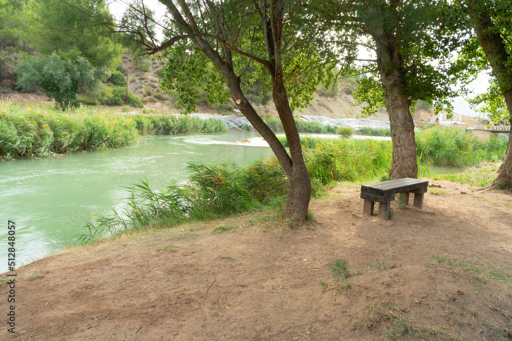 a wooden bench in the forest next to the river, the wooden long chair under the trees, the bench next to the peaceful river a wooden bench in the forest next to the river, the wooden long chair under the trees, the bench next to the peaceful river