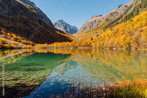 Lake with transparent water and autumnal trees. Mountains and lake