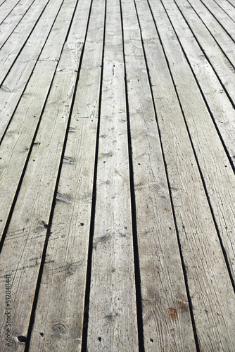 Closeup of a wooden plank surface. Light grey vintage flooring with slats forming an outdoor terrace. Old textures of hard wood floor used as a walkway or deck. Long vertical outdoor floorboards