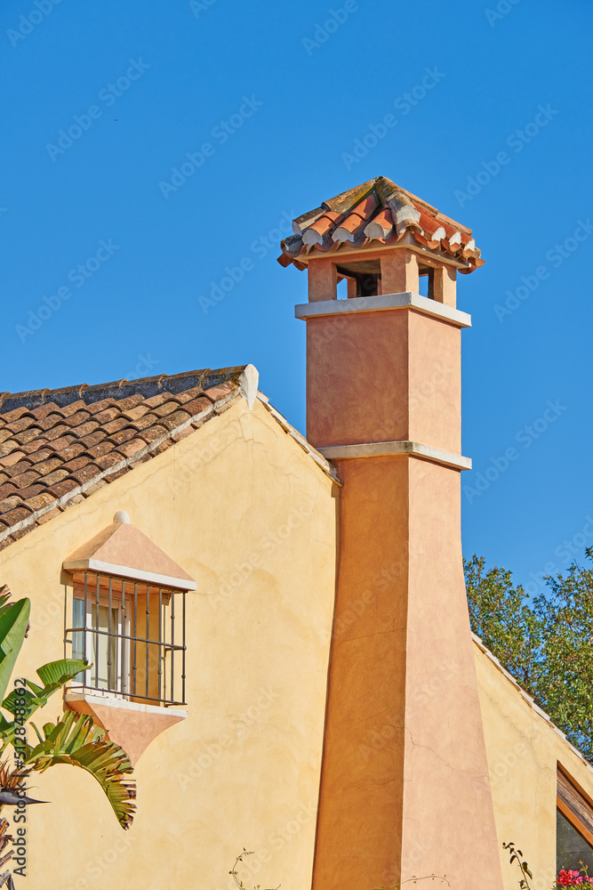 Chimney designed on roof of orange painted house building outside against blue sky background. Construction of exterior architecture of escape chute built on rooftop for fireplace smoke and heat