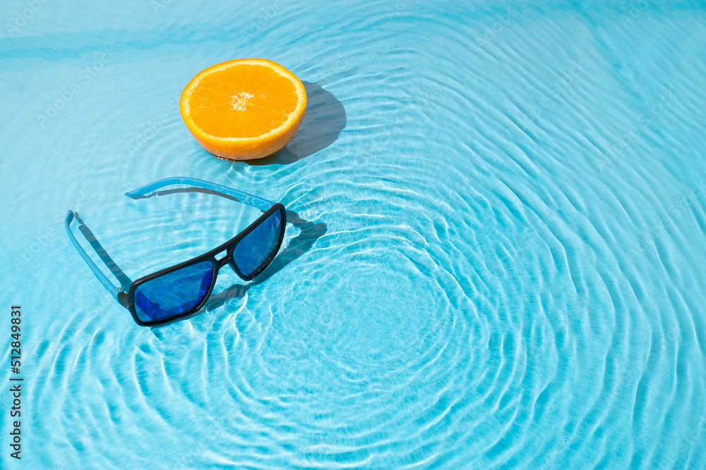 Trendy sunny scene with sunglasses and a slice of orange on a water surface. Summer travel concept. Minimal beach idea. Trendy sunny scene with sunglasses and a slice of orange on a water surface. Summer travel concept. Minimal beach idea.