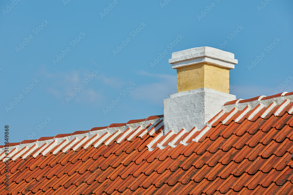 Fototapeta premium Brick chimney designed on slate roof of house building outside against blue sky background. Construction of exterior architecture of escape chute built on rooftop for fireplace smoke and heat