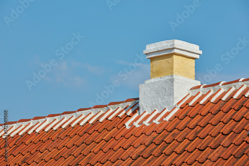 Brick chimney designed on slate roof of house building outside against blue sky background. Construction of exterior architecture of escape chute built on rooftop for fireplace smoke and heat © SteenoWac/peopleimages.com