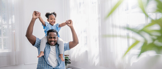 Happy black African American father daughter playing at home living room. Afro man carry piggyback little toddler girl. Cheerful family bonding together father’s day concept banner with copy space