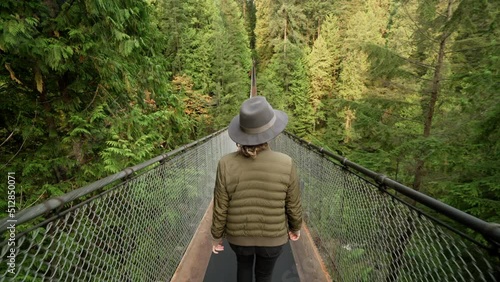 Female tourist wearing a hat, walking along famous suspension bridge in lush rainforest setting in North Vancouver, British Columbia, Canada. 