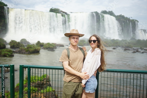 In the photo, a beautiful girl and a guy stand against the backdrop of Iguazu Waterfalls located on the border of Brazil (Paraná state) and Argentina (Misiones province).