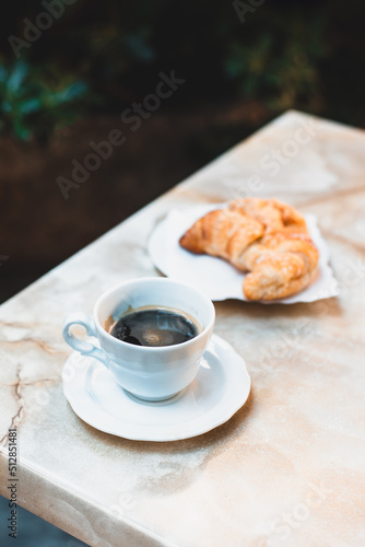 Fototapeta Naklejka Na Ścianę i Meble -  Cup of coffee and a croissant for breakfast on a table in a street cafe.