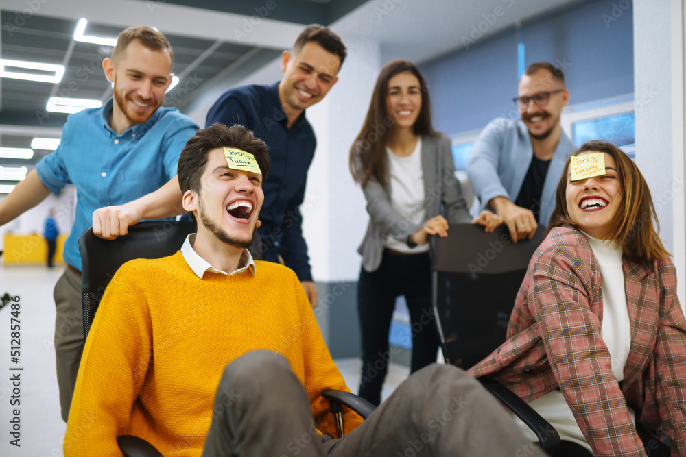 Young cheerful business people racing on office chairs and laughing. Funny activity, celebrating corporate success. Business concept. Young cheerful business people racing on office chairs and laughing. Funny activity, celebrating corporate success. Business concept.