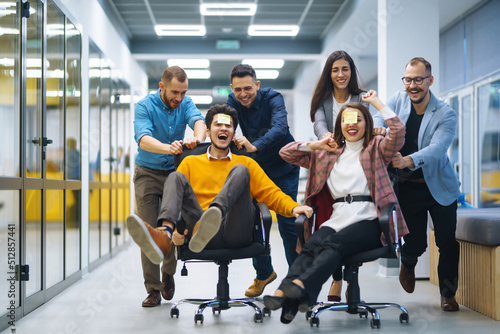Foto Young cheerful business people racing on office chairs and laughing