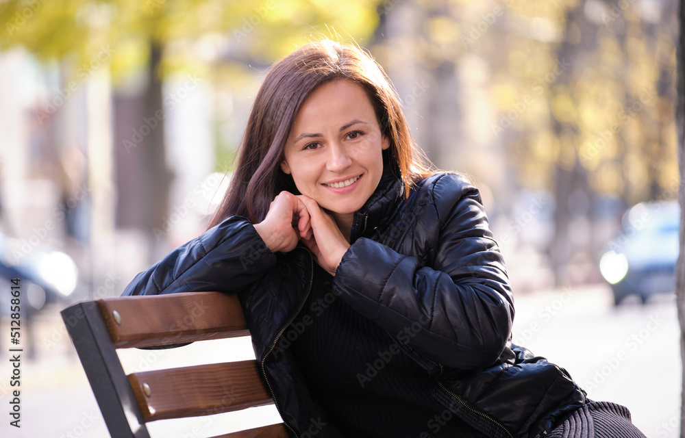 Young happy woman sitting relaxed on street bench on warm autunm day. Wellness and resting from everyday rush concept Young happy woman sitting relaxed on street bench on warm autunm day. Wellness and resting from everyday rush concept