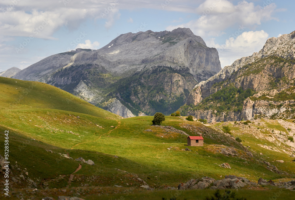 landscape of a mountain meadow with a cabin at the foot of a large rocky peak