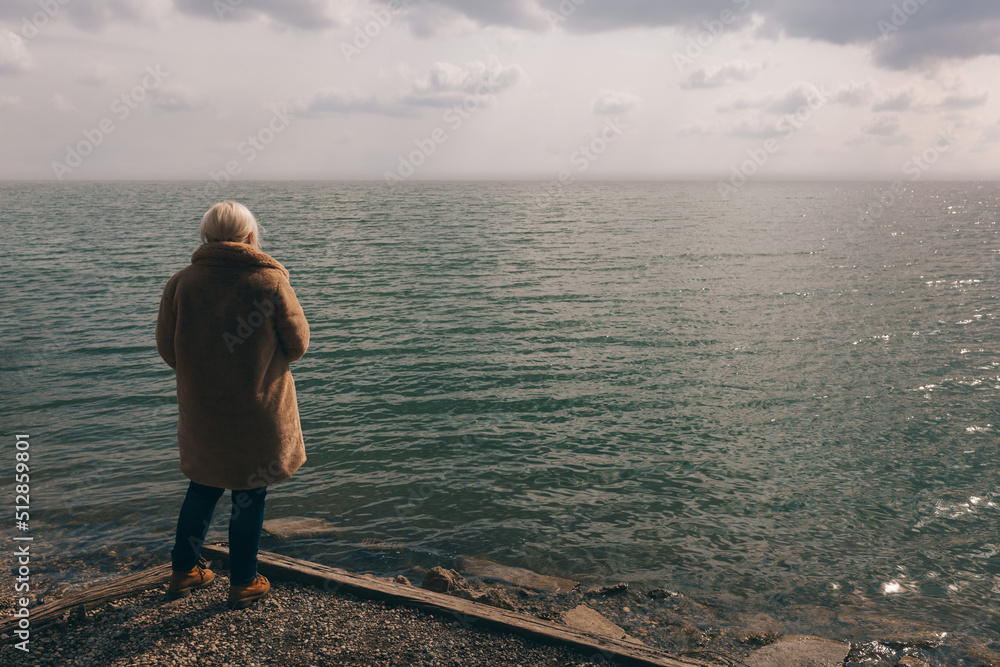 Woman with blonde hair standing alone by the water looking into the distant horizon Woman with blonde hair standing alone by the water looking into the distant horizon