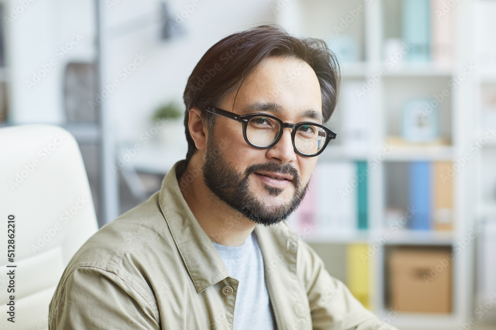 Portrait of content handsome young bearded Asian guy in eyeglasses working in modern office Portrait of content handsome young bearded Asian guy in eyeglasses working in modern office