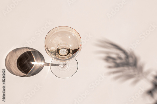 Cocktail glass with drink on the light surface in sunlight with tropical palm leaves shadows. Minimalist creative summer drinks composition. Flat lay, top view image.